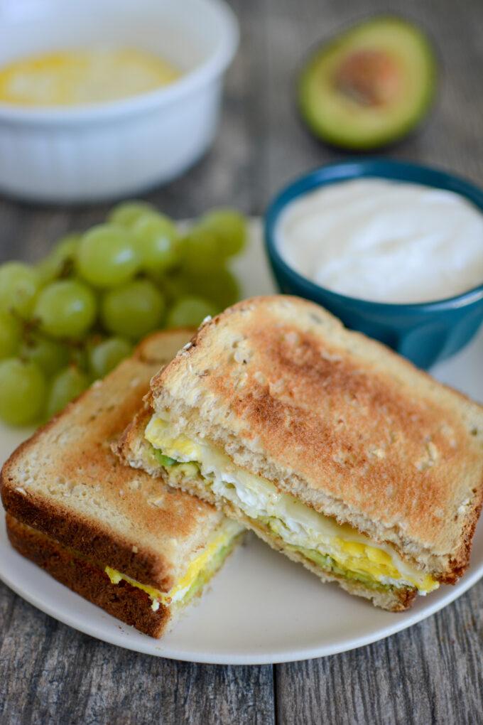 Microwave Egg Sandwich with avocado and cheese and grapes and yogurt on the side