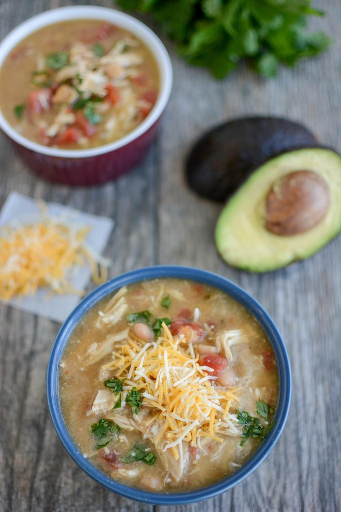 Two bowls of white chicken chili with an avocado and cheese and cilantro