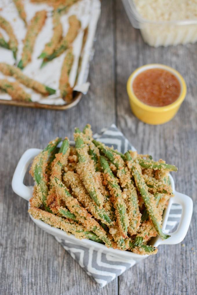 Crispy Green Bean Fries in a white dish and on a sheetpan with Italian Dressing for dipping