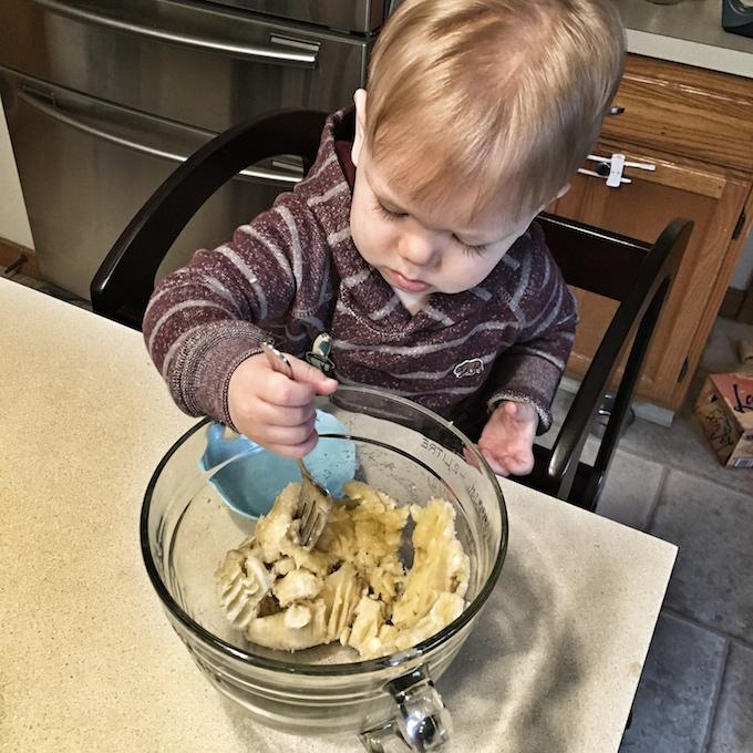 toddler in the kitchen mashing banana