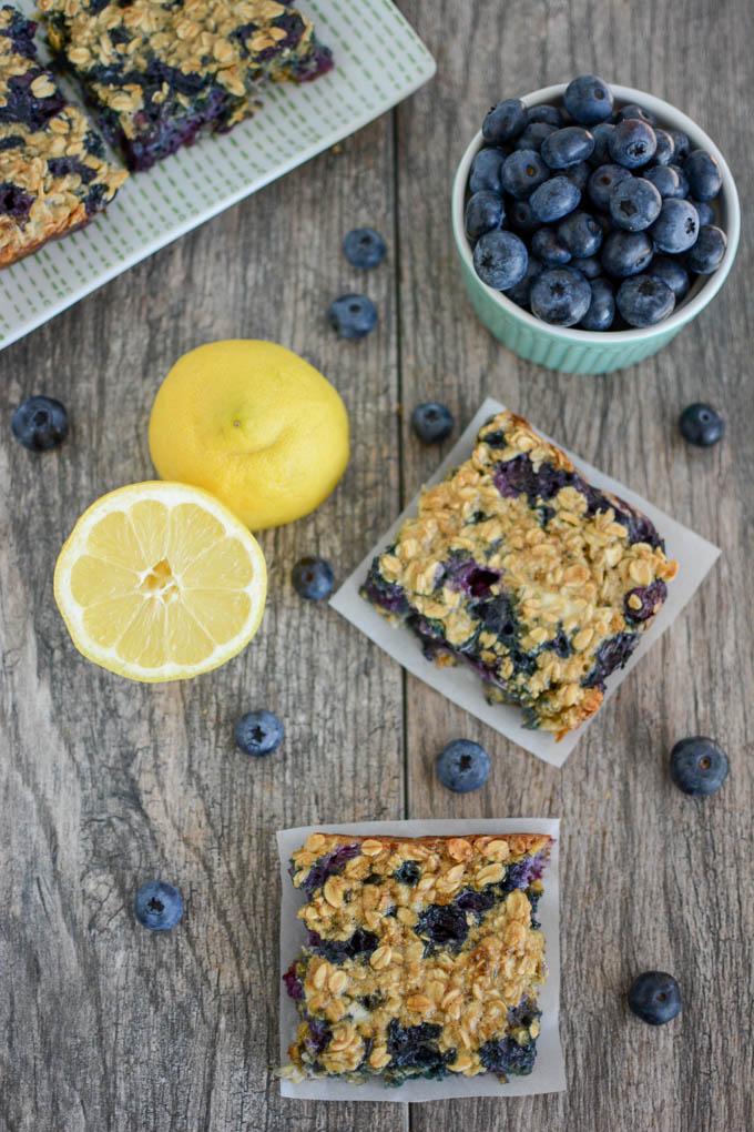 Lemon Blueberry Cheesecake Oat Bars overhead with lemon cut in half and bowl of blueberries