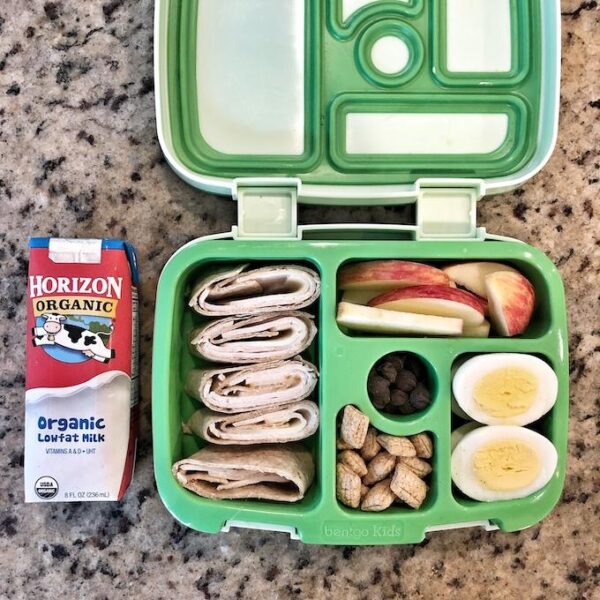 Packed lunch with horizon organic shelf stable milk, turkey rollup, apple, barbaras puffins, hard boiled eggs