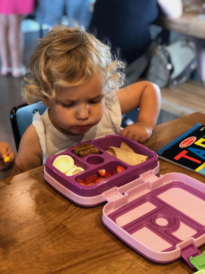 toddler eating quesadilla and hard boiled egg out of lunch box