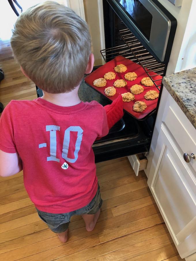 kid putting cookies in the oven