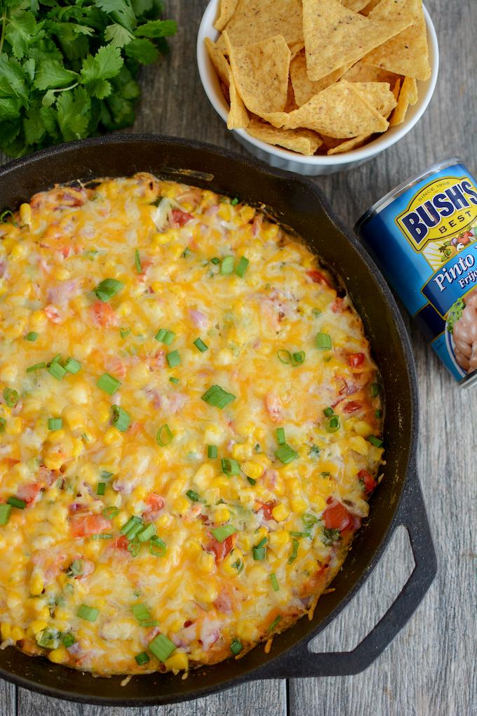 Hot Taco Layer Dip in a cast iron skillet with chips and a can of pinto beans