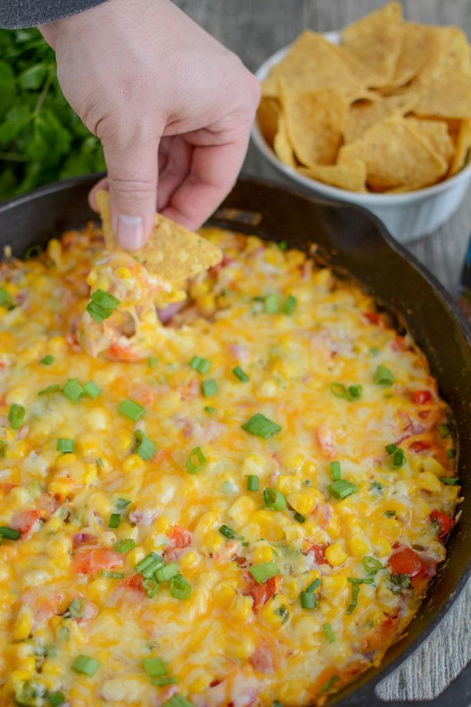 hand dipping into skillet of hot taco layer dip with bowl of chips