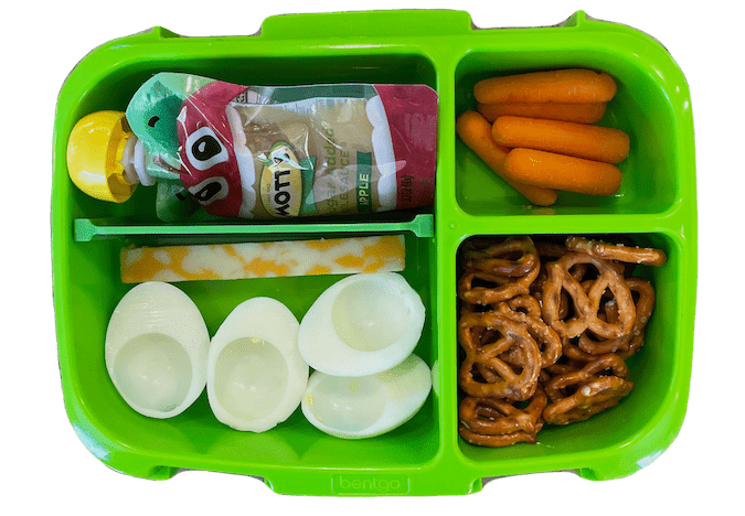 kids lunch box with applesauce, carrots, cheese stick, hard boiled egg and pretzels