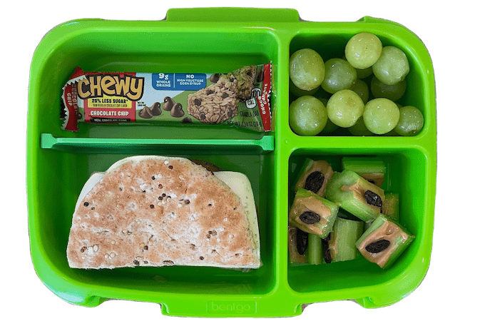 almuerzo para niños con barra de granola, sándwich de pavo, uvas y hormigas en un tronco